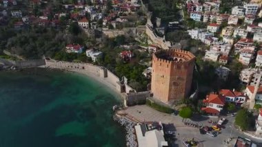 Alanya 'nın küçük limanındaki kırmızı kuleye hayran olun. Arkasında taş duvarlar ve yüksek bir dağ var..