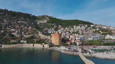 Alanya 'nın deniz kenarındaki kırmızı kulesini ziyaret edin taş duvarları ve nefes kesici dağ manzaralı çarpıcı bir yapı..