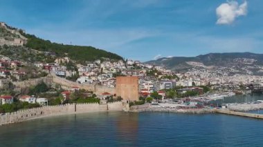 Alanya 'nın limanındaki kırmızı kuleyi keşfedin. Arkasında taş mimarisi ve görkemli bir dağ var..