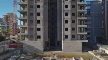 Yüksek beton binanın en üst katlarında işçiler görülüyor..