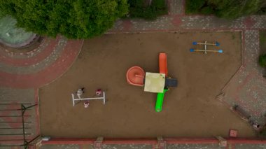 Çocuklar sallanırken, yetişkinler oyun alanında gözetmenlik yapıyor..