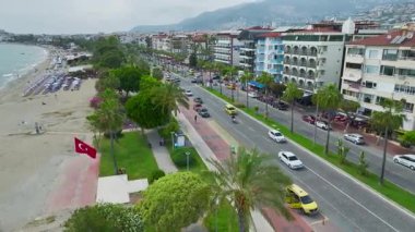 Araçlar, sahil ve palmiye ağaçlarının yanındaki işlek bir caddede ilerliyor..