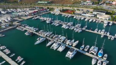 Güneşli gökyüzünün altında yelkenli ve katamaranlarla dolu modern bir yat limanının havadan görünüşü.