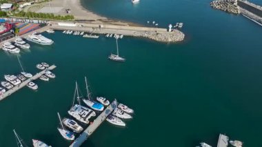 Güneşli gökyüzünün altında yelkenli ve katamaranlarla dolu modern bir yat limanının havadan görünüşü.