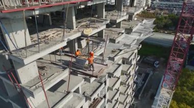 Turna kolu ufuk çizgisi boyunca uzanıyor. İşçiler arka planda mavi deniz olan güçlendirilmiş paneller kuruyor..