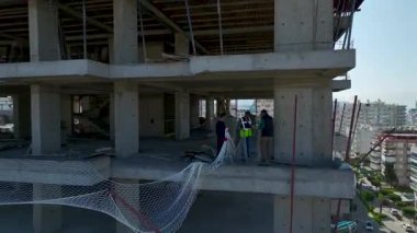 İnsansız hava aracı bitmemiş inşaat alanının üzerinde malzeme, yapı iskelesi ve işçilerle uçuyor..