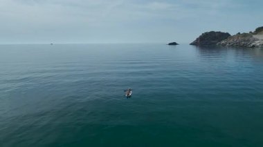 İki kişi sessizce turkuaz sularda yüzüyor ve arkada kayalıklar var..