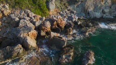 Yeşil tepeli ve kayalıklı deniz kenarındaki evlerin insansız hava aracı görüntüsü