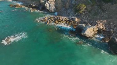 Dalgalar dalgalanır engebeli kayalık kıyı şeridinde.