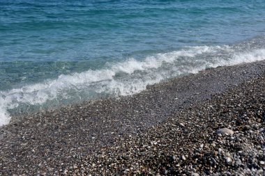 Arka planda deniz ve kumsal olan çakıl taşları bankası. Türkiye 'de Kemer, Antalya' da deniz kıyısında çakıl ve su