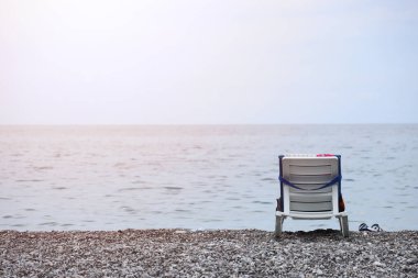 Arka planda deniz ve plaj olan çakıl taşlarının üzerinde plastik sandalye. Türkiye 'de Kemer, Antalya' da deniz kıyısında çakıl ve su