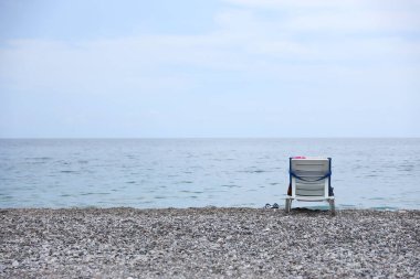 Arka planda deniz ve plaj olan çakıl taşlarının üzerinde plastik sandalye. Türkiye 'de Kemer, Antalya' da deniz kıyısında çakıl ve su