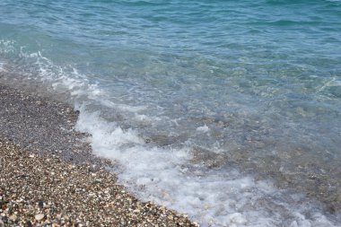 Arka planda deniz ve kumsal olan çakıl taşları bankası. Türkiye 'de Kemer, Antalya' da deniz kıyısında çakıl ve su