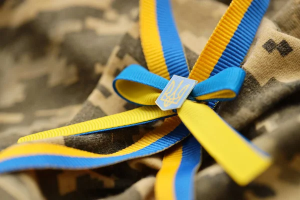 stock image Pixeled digital military camouflage fabric with ukrainian flag and coat of arms on stripes ribbon in blue and yellow colors. Attributes of ukrainian soldier uniform