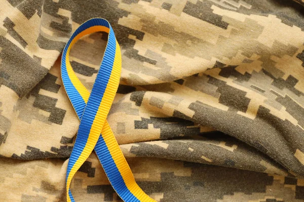 Stock image Pixeled digital military camouflage fabric with ribbon in blue and yellow colors. Attributes of ukrainian patriotic soldier uniform