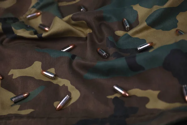 Many pistol bullets and cartridges on dark camouflage background. Concept of war action or hunting