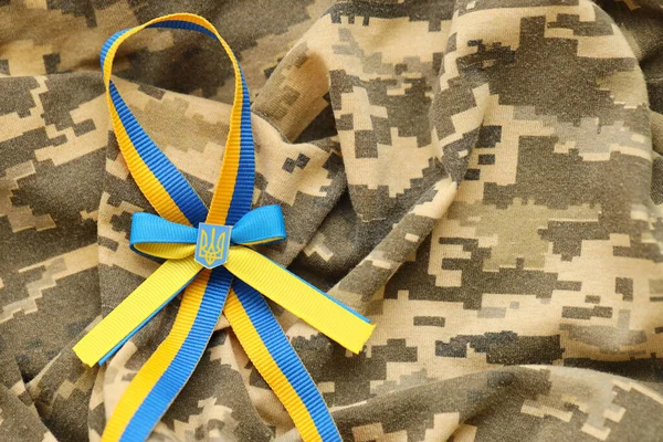 stock image Pixeled digital military camouflage fabric with ukrainian flag and coat of arms on stripes ribbon in blue and yellow colors. Attributes of ukrainian soldier uniform