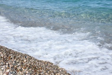 Arka planda deniz ve kumsal olan çakıl taşları bankası. Türkiye 'de Kemer, Antalya' da deniz kıyısında çakıl ve su