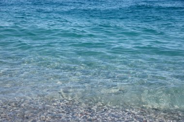 Arka planda deniz ve kumsal olan çakıl taşları bankası. Türkiye 'de Kemer, Antalya' da deniz kıyısında çakıl ve su