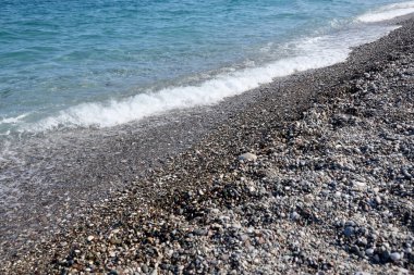 Arka planda deniz ve kumsal olan çakıl taşları bankası. Türkiye 'de Kemer, Antalya' da deniz kıyısında çakıl ve su