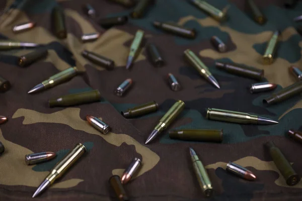 stock image Many rifle bullets and cartridges on dark camouflage background. Concept of war action or hunting