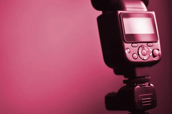 External photographic flash is mounted on the synchronizer, which stands on a tripod. lighting equipment objects. Image toned in Viva Magenta, color of the 2023 year