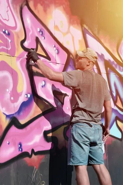 年轻的高加索男性涂鸦画家用蓝色和粉色的色调画大型街头艺术画 穿着粗斜纹棉布短裤和灰色T恤的时髦男子在阳光灿烂的天气里在户外制作了新的石棺艺术 — 图库照片