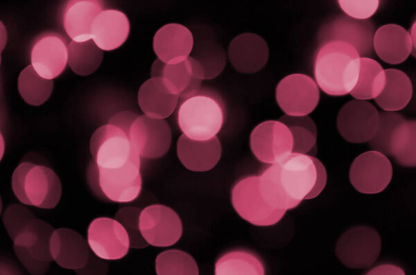 Abstract background image with bokeh effect. Many brightly ed circular shapes on a dark background. Image toned in Viva Magenta, color of the 2023 year