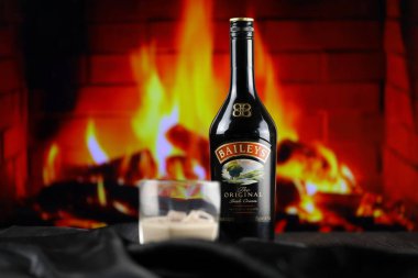 KYIV, UKRAINE - 4 Mayıs 2022 Baileys orijinal alkol şişesi ahşap masada, arka planda kırmızı şömine var. Elit alkol üretimi