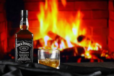 KYIV, UKRAINE - MAY 4, 2022 Jack Daniels original alcohol bottle on wooden table with red fireplace on background. Elite alcohol production