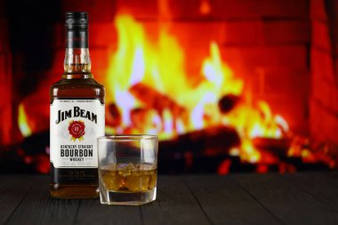 KYIV, UKRAINE - MAY 4, 2022 Jim Beam original alcohol bottle on wooden table with red fireplace on background. Elite alcohol production