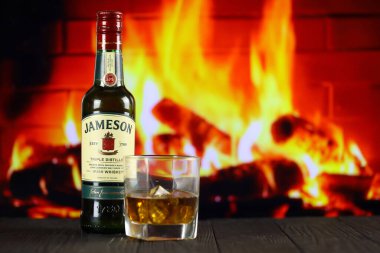 KYIV, UKRAINE - 4 Mayıs 2022 Jameson orijinal alkol şişesi ahşap masada, arka planda kırmızı şömine var. Elit alkol üretimi