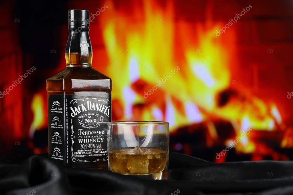KYIV, UKRAINE - MAY 4, 2022 Jack Daniels original alcohol bottle on wooden table with red fireplace on background. Elite alcohol production