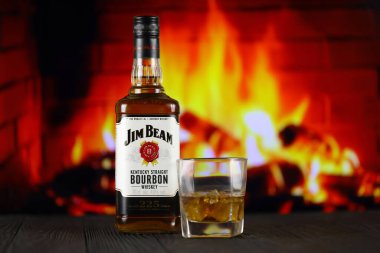 KYIV, UKRAINE - MAY 4, 2022 Jim Beam original alcohol bottle on wooden table with red fireplace on background. Elite alcohol production