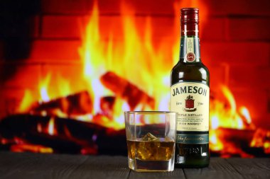 KYIV, UKRAINE - 4 Mayıs 2022 Jameson orijinal alkol şişesi ahşap masada, arka planda kırmızı şömine var. Elit alkol üretimi