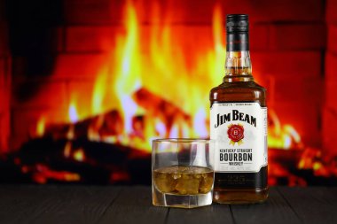 KYIV, UKRAINE - MAY 4, 2022 Jim Beam original alcohol bottle on wooden table with red fireplace on background. Elite alcohol production