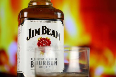 KYIV, UKRAINE - MAY 4, 2022 Jim Beam original alcohol bottle on wooden table with red fireplace on background. Elite alcohol production