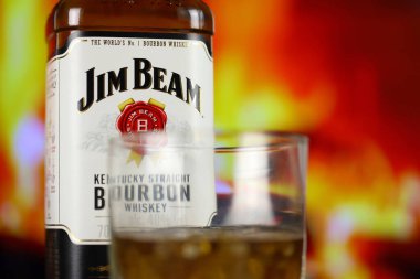 KYIV, UKRAINE - MAY 4, 2022 Jim Beam original alcohol bottle on wooden table with red fireplace on background. Elite alcohol production