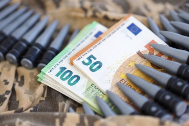 Avro banknotları ve Ukraynalı bir askerin kamuflaj üniformasında bir makineli tüfek kemeri. Savaş finansmanı, rüşvet ya da bağış kavramı. Ukrayna 'ya ABD' den yardım