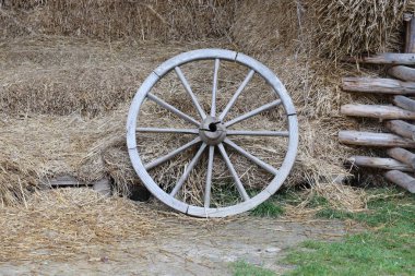 Yığınla saman küpü ve eski el arabasının ahşap tekerlekleri olan bir yer.
