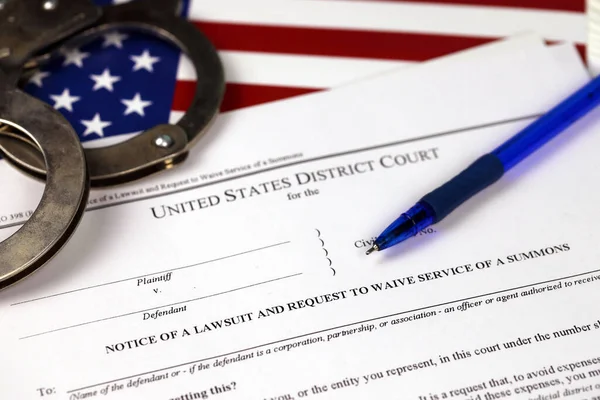 District court Notice of the lawsuit and request to waive service of a summons. Papers with handcuffs and blue pen on United States flag close up