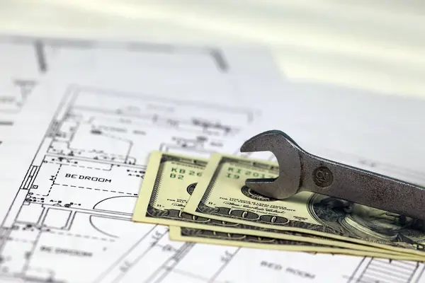 Spanner on top of money with blueprints of residential house plan. Restoring, repair, service maintenance cost concept