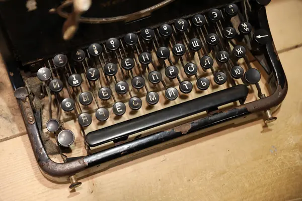 Details of an old retro typewriter in vintage style with dusty surfaces on wooden table in dark interior