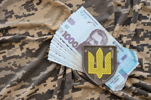 Ukrainian army symbol and bunch of hryvnia bills on military uniform. Payments to soldiers of the Ukrainian army, salaries to the military. War in Ukraine