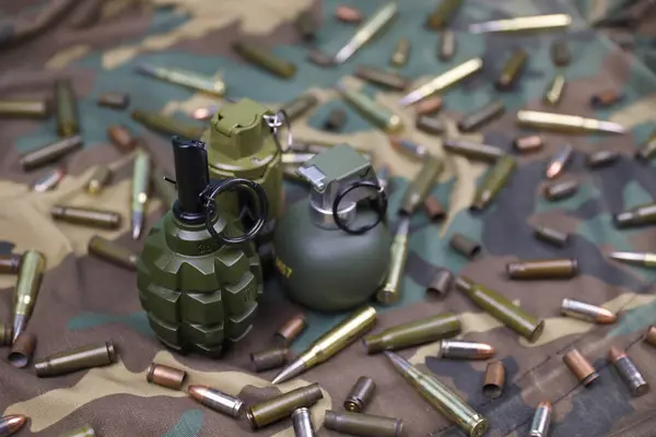 Different types of ammunition and grenades on a camouflage background. Preparing for war. Possession of weapons