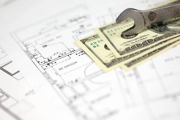 Spanner on top of money with blueprints of residential house plan. Restoring, repair, service maintenance cost concept