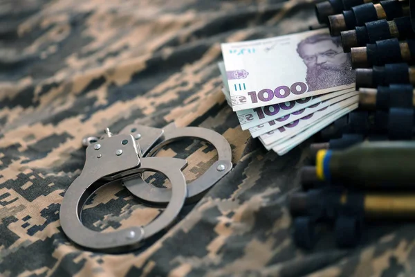 Ukrainian army machine gun belt shells, handcuffs and bunch of hryvnia bills on military uniform. Concept of bribery and war crimes during war in Ukraine