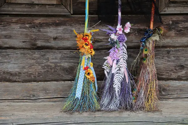 Three different brooms of witches stand at the old wooden hut house close up