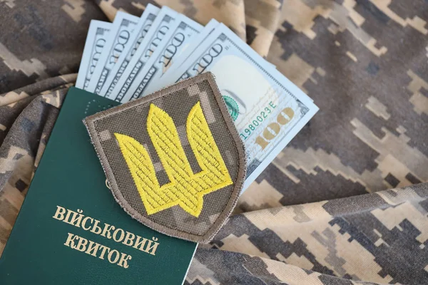 Symbol of Ukrainian army and military ID with bunch of money on the camouflage uniform of a Ukrainian soldier. Concept of payment to military personnel or bribe for deferment from military service