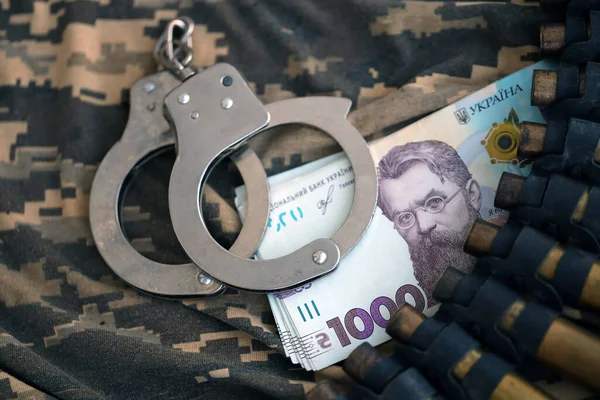 Ukrainian army machine gun belt shells, handcuffs and bunch of hryvnia bills on military uniform. Concept of bribery and war crimes during war in Ukraine